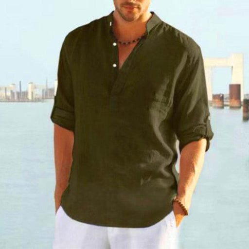 Man wearing a dark green shirt with rolled-up sleeves by a waterfront with a bridge in the background.