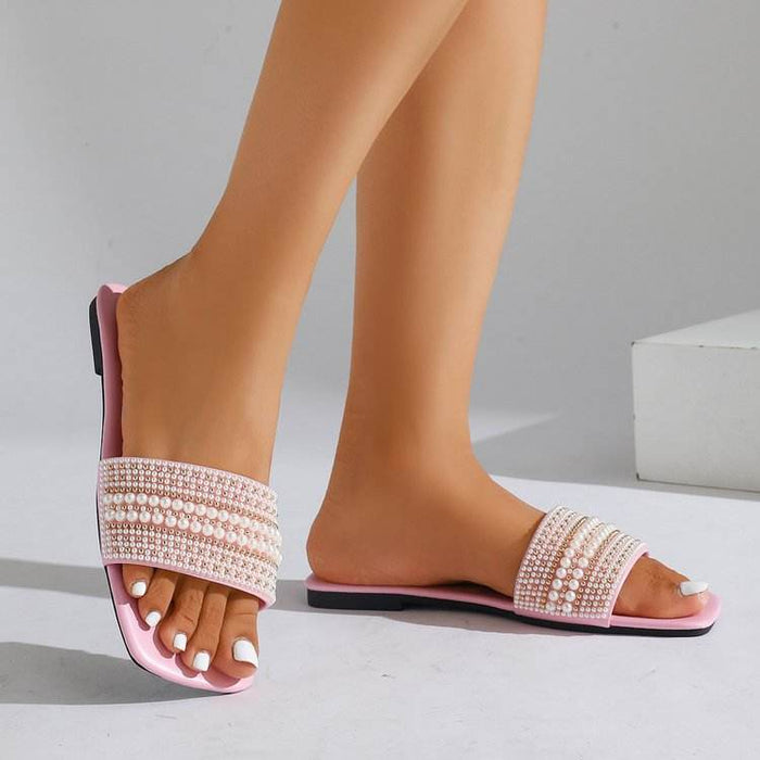 Pink sandals with pearl embellishments worn by a person on a neutral background