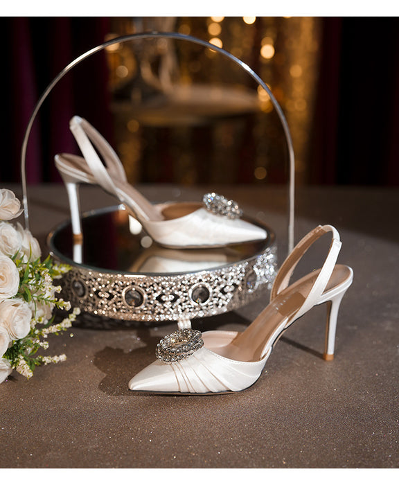 White high-heeled shoes with decorative elements on a decorative stand with flowers in the background.