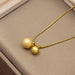 A gold necklace with two spherical pendants, one textured and one smooth, displayed on a beige jewelry box.