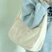 Beige shoulder bag held by a person wearing a gray sweatshirt against a light green background