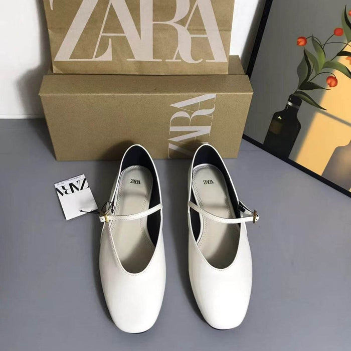 White shoes with gold straps in front of a Zara box on a gray surface.