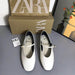 White shoes with gold straps in front of a Zara box on a gray surface.