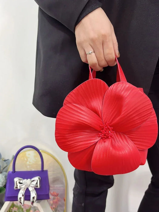 Red floral-shaped handbag held by a person against a white background