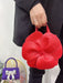 Red floral-shaped handbag held by a person against a white background