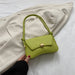Green handbag on a white surface with a beige coat