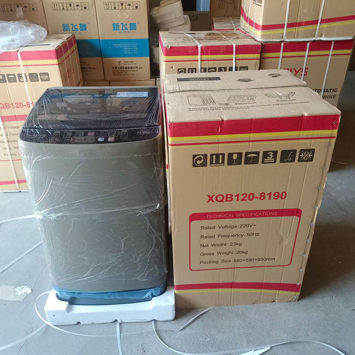 Washing machine next to its packaging box with specifications on a warehouse floor.