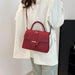 A person wearing a white blazer and light blue jeans carries a structured red handbag with a crocodile-embossed texture, top handle, and shoulder strap.