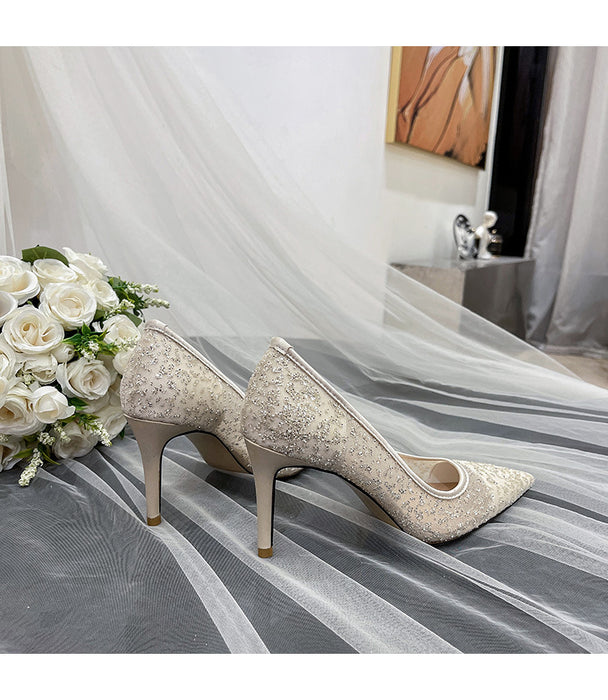 Pair of glittery high-heeled shoes on a white fabric background with flowers and a mirror.