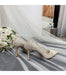 Pair of glittery high-heeled shoes on a white fabric background with flowers and a mirror.