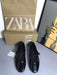 Black shoes with a Zara box on a gray surface