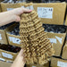 Blonde hair extensions held by a hand with stacked boxes in the background