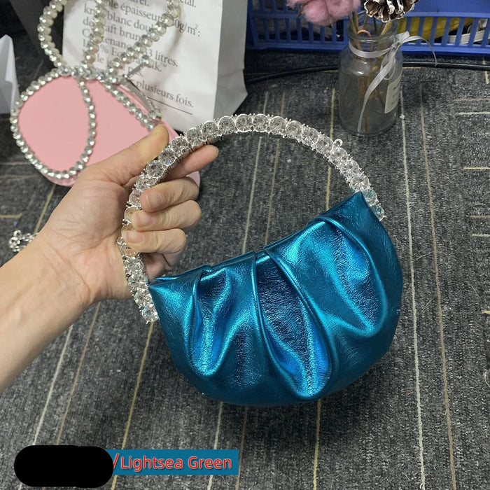 Blue handbag with crystal handle held by a hand on a textured surface.