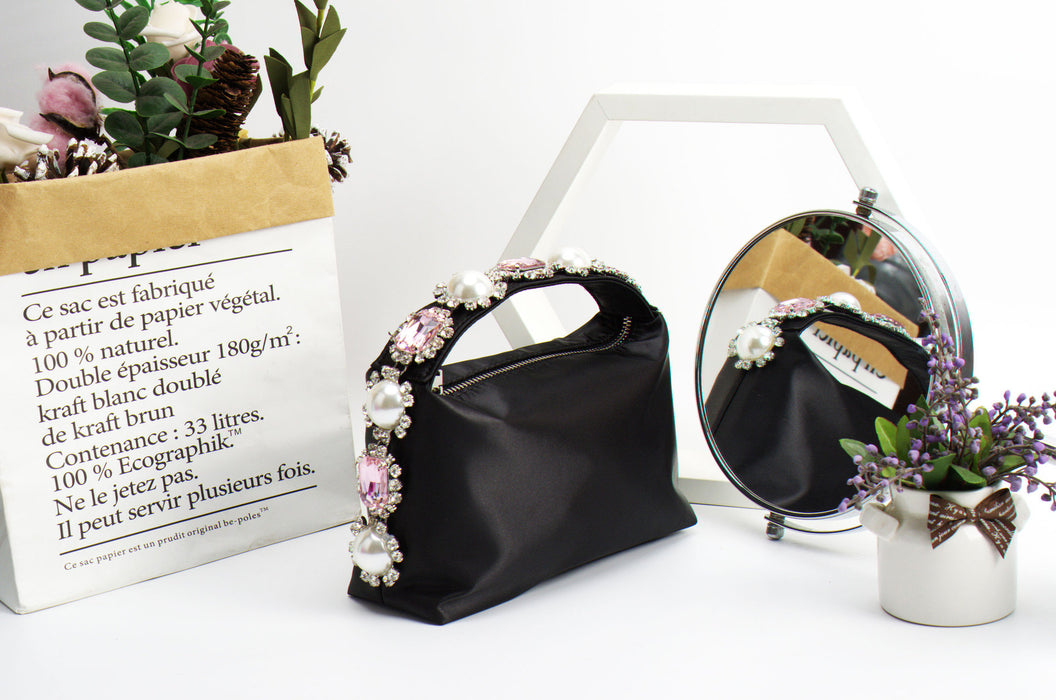 Black handbag with floral decorations on a white surface with a mirror and plant in the background.