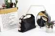 Black handbag with floral decorations on a white surface with a mirror and plant in the background.