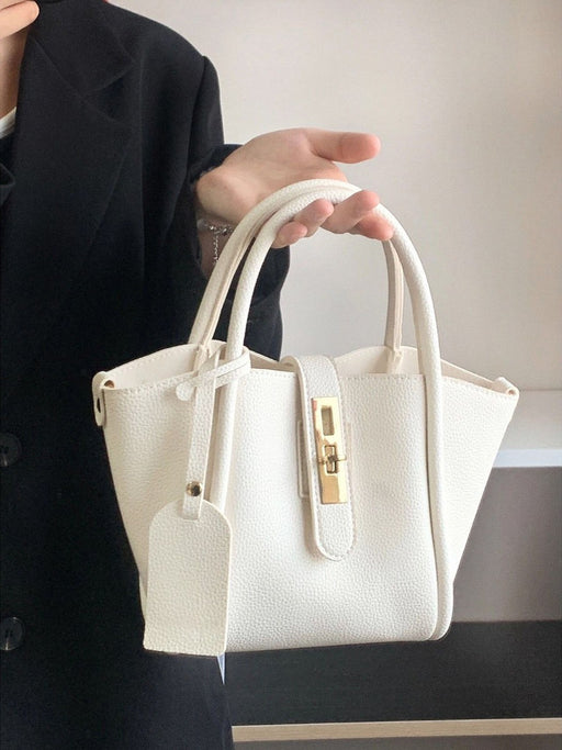 White handbag held by a person wearing a black coat against a neutral background
