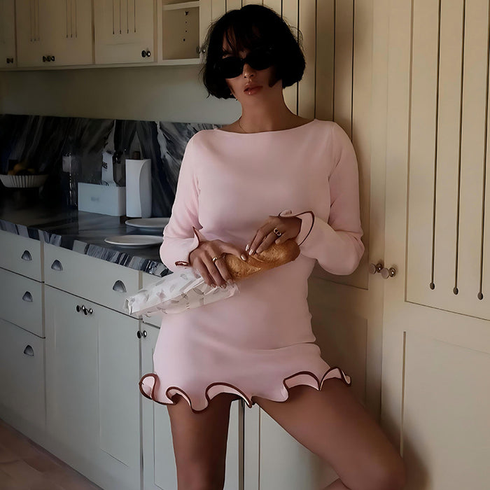 Woman in a pink dress holding a baguette in a kitchen.
