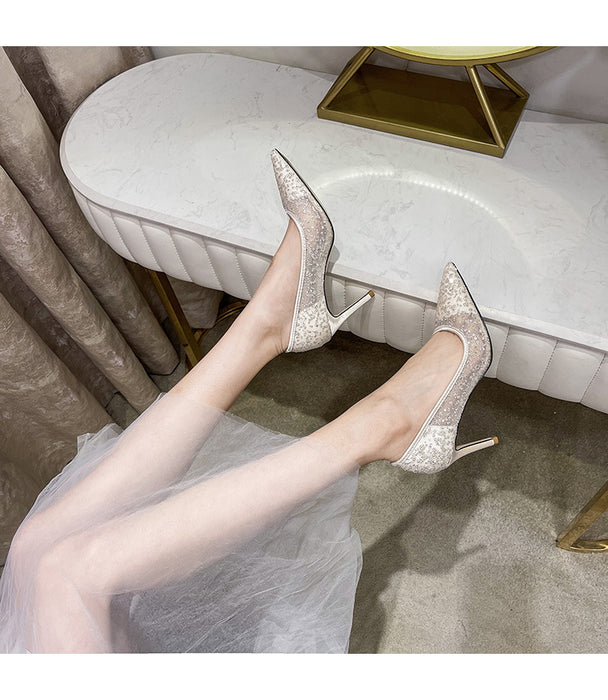Silver high-heeled shoes worn by a person sitting on a white chair.