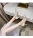 Silver high-heeled shoes worn by a person sitting on a white chair.