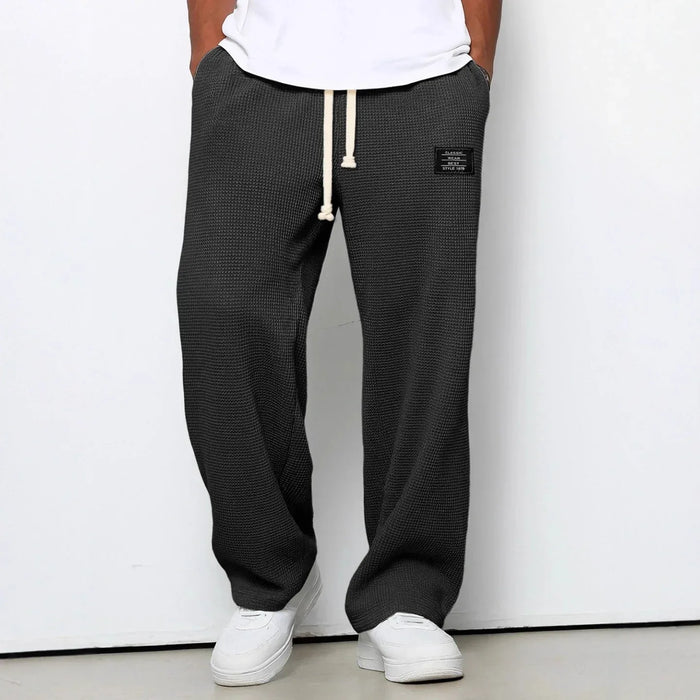 Person wearing black checkered pants with a white label on a plain background