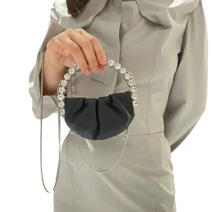 Person holding a black handbag with decorative chain and embellishments