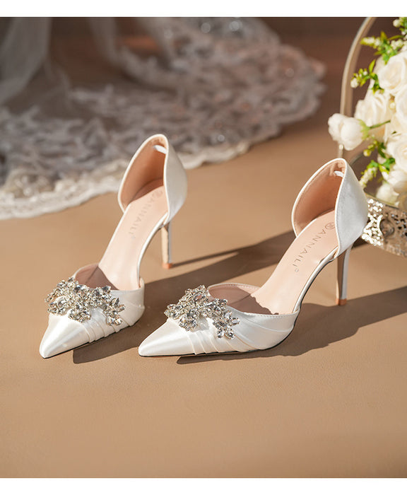 White high-heeled shoes with embellishments on a beige surface.