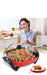Woman in a kitchen with a large cooking pot containing food, smiling at the camera.