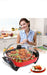Woman in a kitchen with a large cooking pot containing food, smiling at the camera.