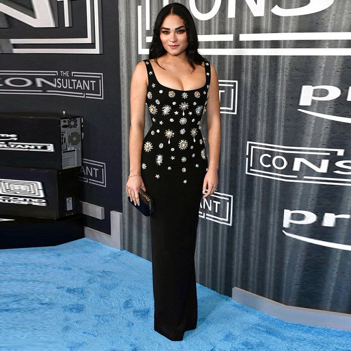 Woman in a black dress with white embellishments on a blue carpet at an event.