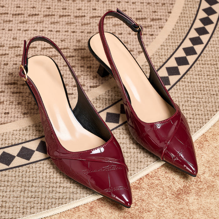 A pair of glossy pointed-toe slingback pumps in deep burgundy with a crocodile-embossed texture and low kitten heels, displayed on a patterned beige rug.