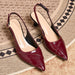 A pair of glossy pointed-toe slingback pumps in deep burgundy with a crocodile-embossed texture and low kitten heels, displayed on a patterned beige rug.