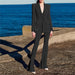 Person wearing a black suit standing on a stone ledge with ocean in the background