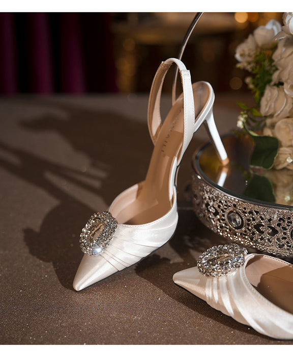 White high-heeled shoes with decorative brooches on a reflective surface.
