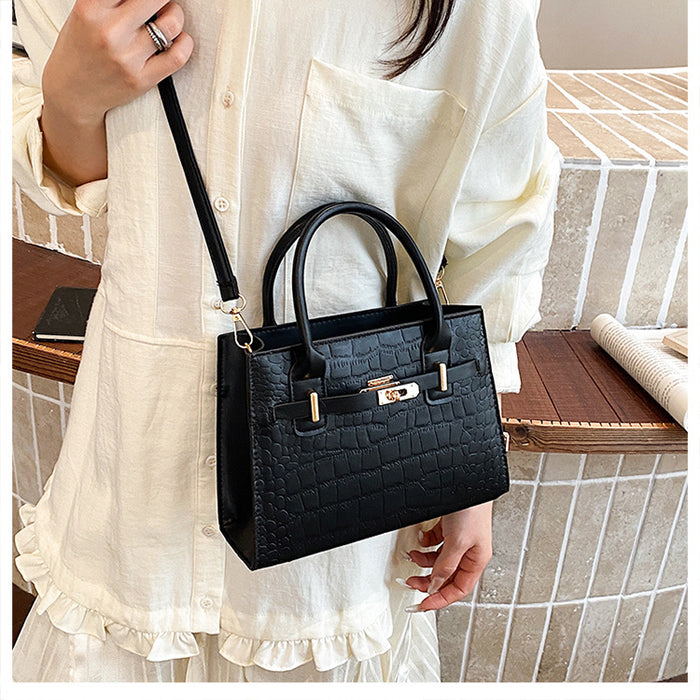 A woman wearing a cream-colored linen shirt holds a black crocodile-embossed mini handbag with gold-tone hardware and a shoulder strap.