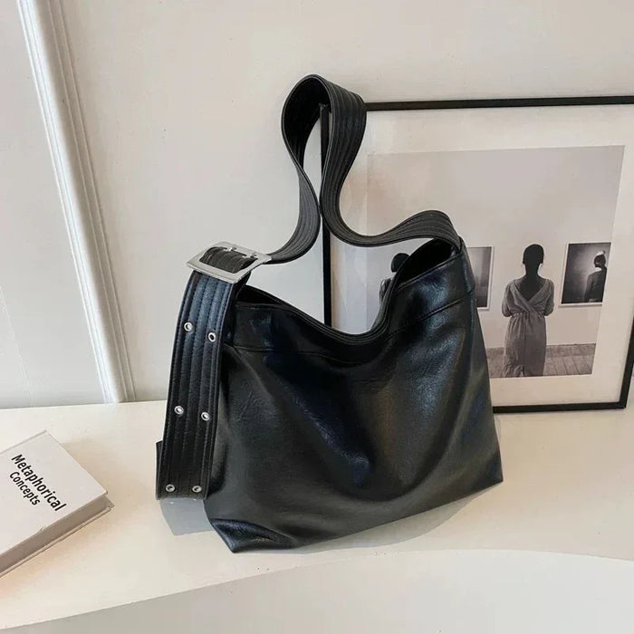 Black leather handbag on a white surface with a framed picture in the background