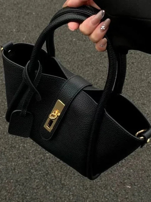 Black handbag with a gold clasp held by a hand on a dark background