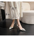 White high-heeled shoes with embellishments worn by a person sitting on a couch.