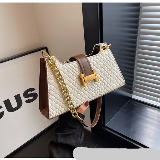 White textured handbag with gold chain and brown strap held by a person, with a blurred background.