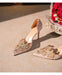Pair of embellished high-heeled shoes on a textured surface with flowers in the background.