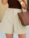 Person wearing beige shorts and a brown top, holding a brown handbag.