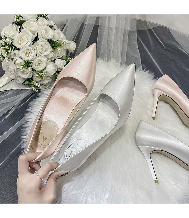 Pair of high-heeled shoes with a bouquet of white roses on a soft fabric background
