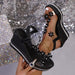 Black wedge sandals with floral embellishments held against a glittery background