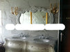 Luxurious bathroom vanity with ornate mirror and wall sconces against a marble wall.