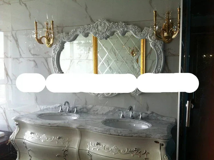 Luxurious bathroom vanity with ornate mirror and wall sconces against a marble wall.