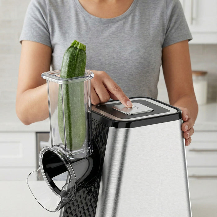 Person using a kitchen appliance with a zucchini in the container, likely a food processor or blender.