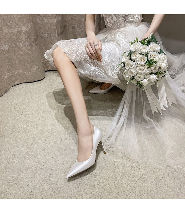Bride in a white lace dress with white shoes holding a bouquet on a neutral background