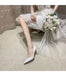 Bride in a white lace dress with white shoes holding a bouquet on a neutral background