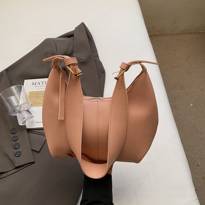 A blush pink leather shoulder bag with gold-tone hardware, held over a brown blazer and a small glass on a white surface.