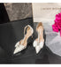 White high-heeled shoes with decorative bows on a black surface, next to a pink flower and 'Choric Koia' box.