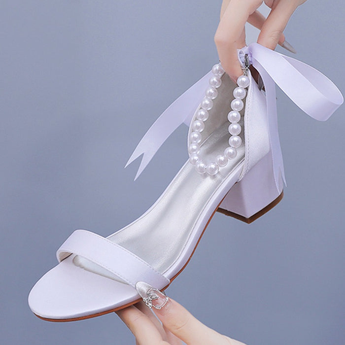 White high-heeled shoe with pearl embellishments on a gray background